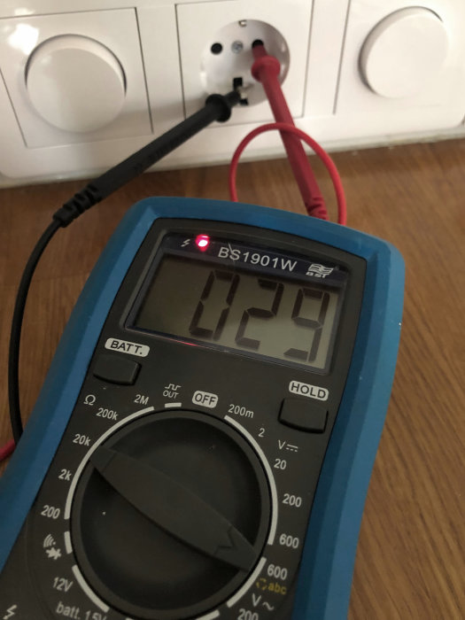 Multimeter som visar 12 V ansluten till ett jordat vägguttag.