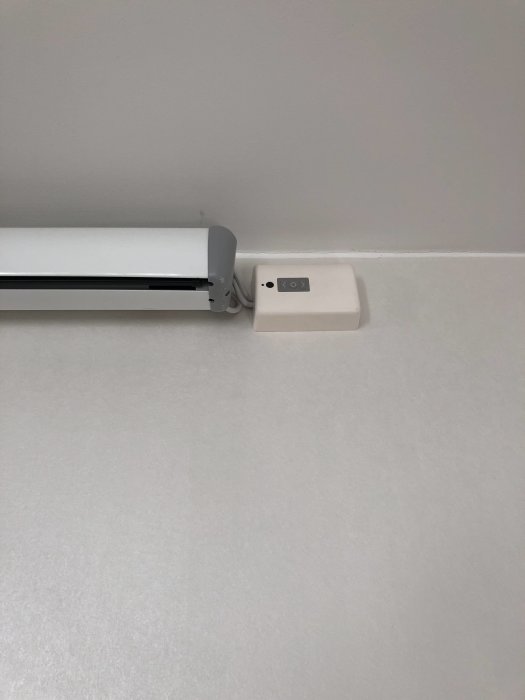 Fibaro shutter installerad i en vit kopplingsdosa på en vägg, bredvid en gardinskena.