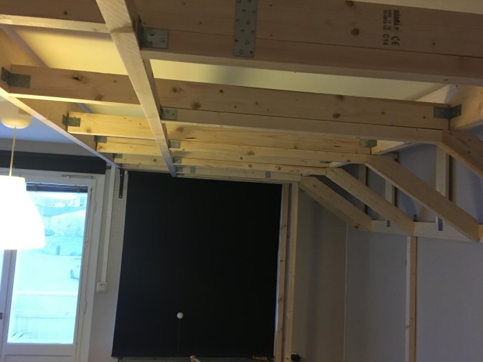 Delvis installerat innertak med träreglar och konsoler i ett rum under renovering.