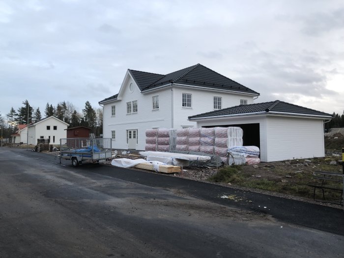 Nybyggt hus med öppen garageport och byggmaterial inklusive isoleringsrullar framför.