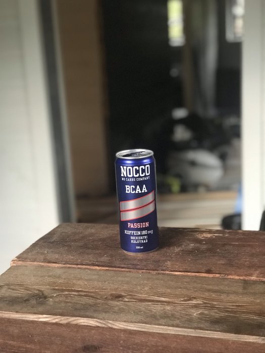 Burk med NOCCO BCAA Passion på en träyta med suddig bakgrund av en byggarbetsplats.