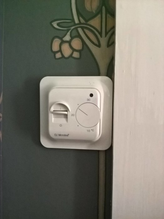 Enkel rumstermostat med vred för temperaturinställning, monterad på vägg.