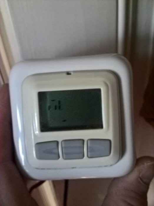 Hand håller en vit termostat med felaktig display som behöver bytas ut.