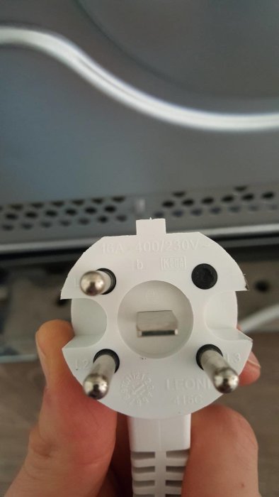 Närbild på en hand som håller en vit PERILEX-kontakt med specifikationer 16A, 400/230V märkta på den.