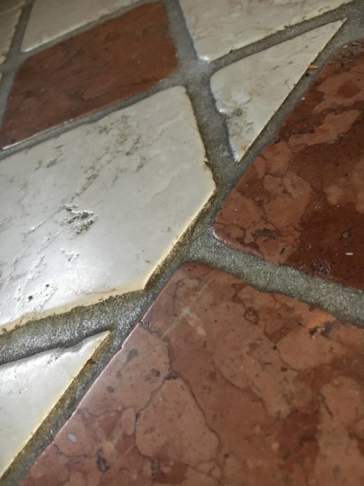 Gammalt ojämnt golv med stora nivåskillnader i sandstensliknande plattor och fogar.