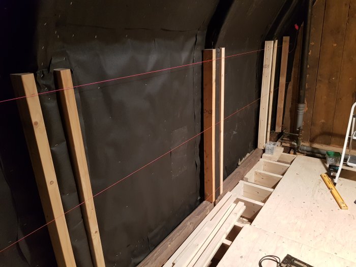 En vägg under konstruktion med röda laserlinjer som markerar räta linjer för riktning av tak och väggar.