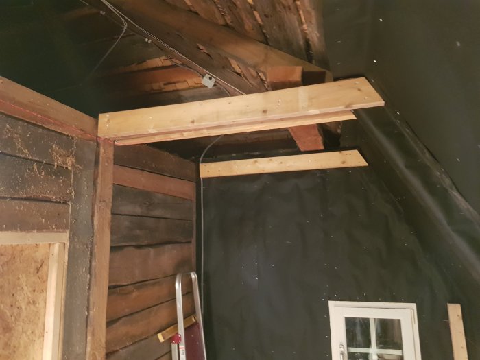 Renovering pågår med exponerade takbjälkar, en röd laserlinje syns över en nyligen uppsatt väggstöd.