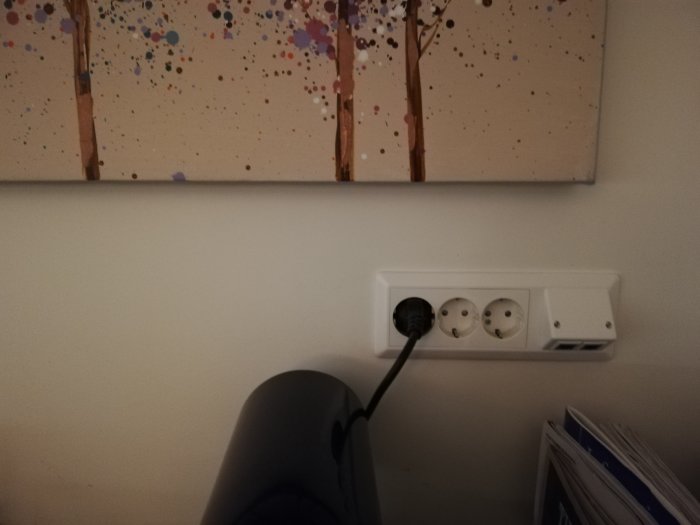 Väggmonterad eluttagspanel med tre uttag och nätverksport under tavla med abstrakt konst.