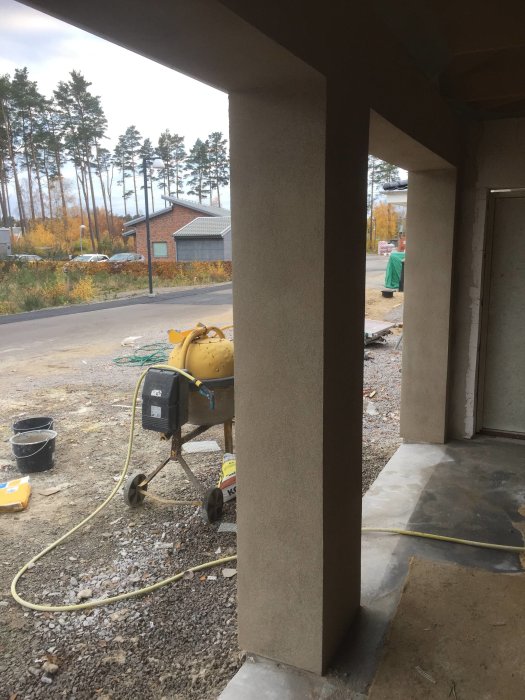 Garage under konstruktion med putsade väggar och synlig betongpelare, omgiven av byggmaterial och en cementblandare.