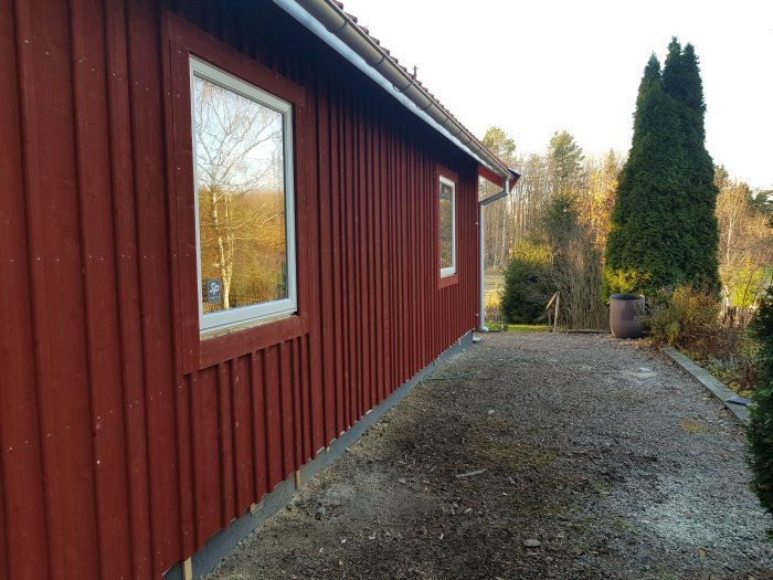 Rödmålat hus med nyinstallerat fönster, omgivet av trädgård och träd.