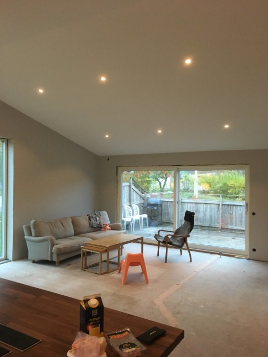 Renoverat vardagsrum med nytt saxtak, inbyggda taklampor och ett öppet skjutparti ut mot terrassen, ofärdigt golv.