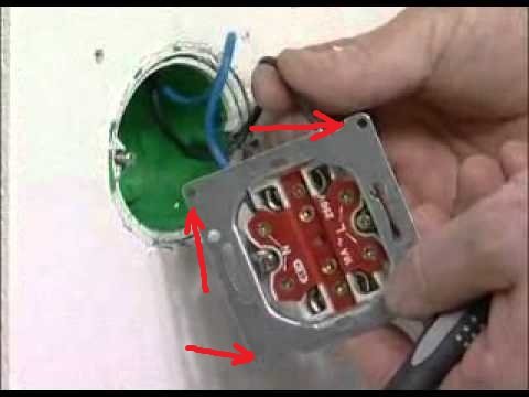 Installation av eluttag med metallram i en vägg där röda pilar pekar på fästpunkter.