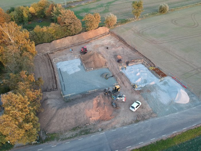 Flygbild av ett byggprojekt med sänkt tomt, stora högar av jord, schaktarbeten, och 800 m utlagd jordvärmeslinga.