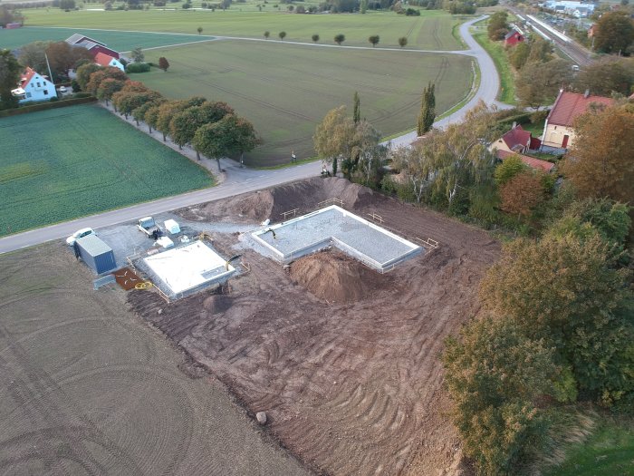 Flygfoto över husgrund på sänkt mark med högar av jord och schakt på tomten.