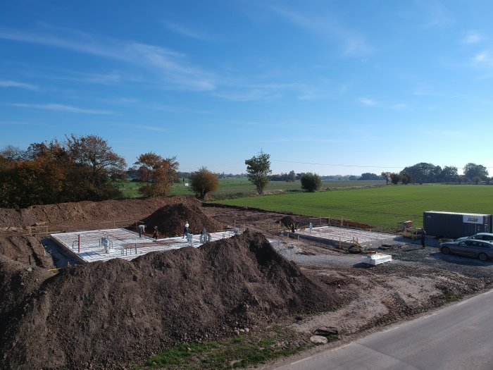 Vy över byggplats med nyligen schaktad jord och pågående grundarbete för hus.