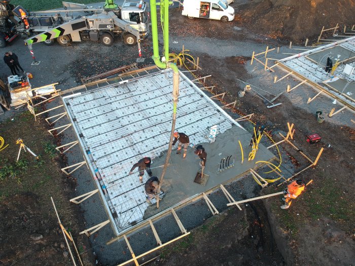 Gjutning av en betongplatta med arbetare, armeringsjärn och en betongpumpbil som häller ut betong.