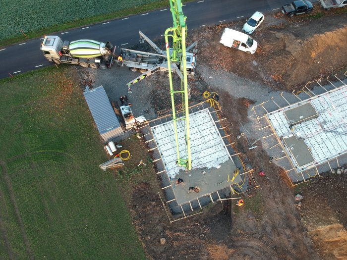 Betonbil häller ut betong på byggplats med fundament och arbetare, sett ovanifrån.