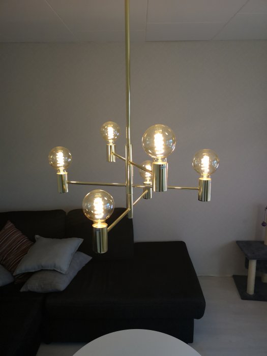 Modern taklampa med sex tända, dimbara LED-glödlampor i ett nyrenoverat vardagsrum med grått och svart tema.