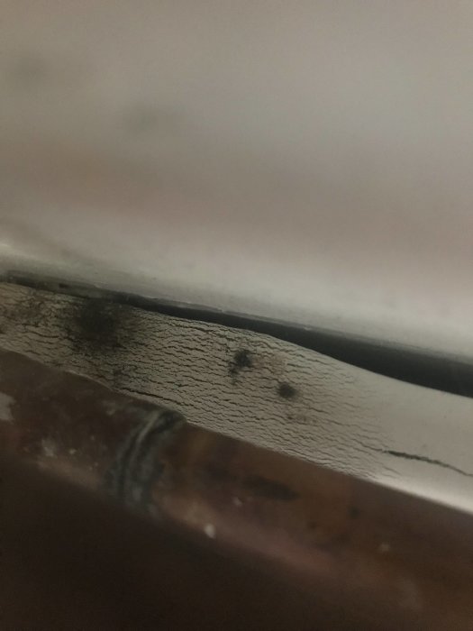 Vattenläckage vid rörskarv intill skadad sockel, synligt fuktiga punkter.