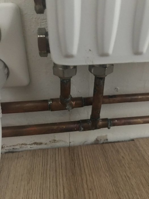 Läckande skarv på ett kopparvattenrör under ett värmelement, med fuktskador på sockeln.