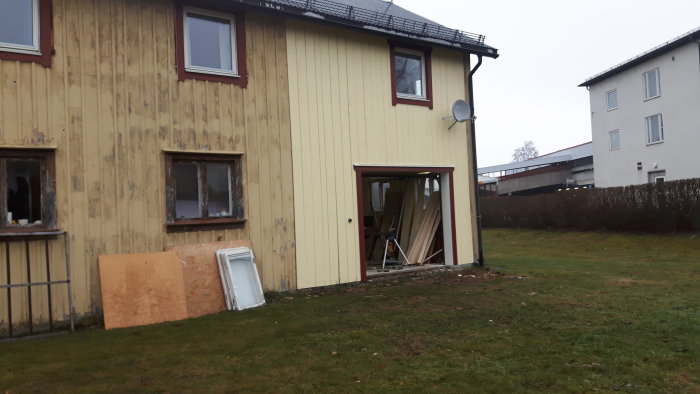 Renoveringsprojekt med halvfärdig fasad, byggmaterial vid öppen port och bortplockade fönster.