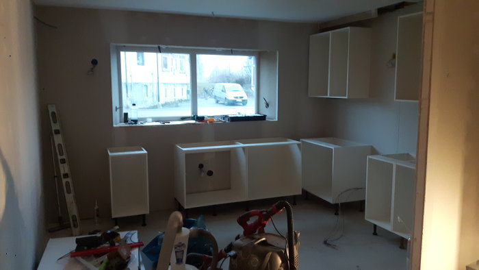 Kök under renovering med vitvaruskåp på plats, kablar synliga, och ouppsatta överskåp.