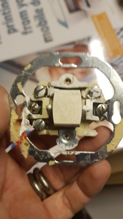 Hand håller en gammal elektrisk brytare med synliga ledningar och skruvanslutningar.