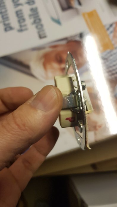 Hand håller en gammal ljusströmbrytare med märkta ledningsterminaler.