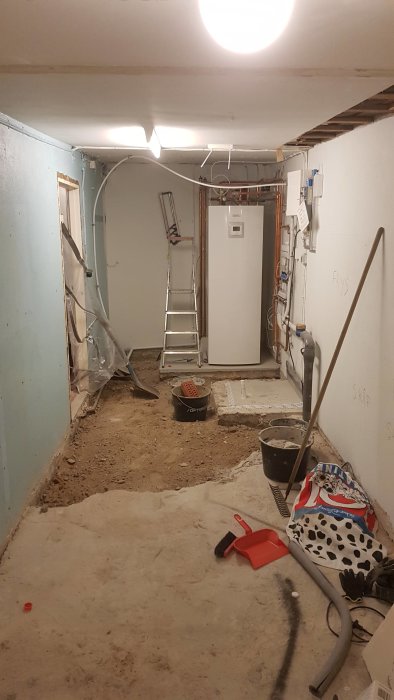 Renoveringsarbete i en oordnad tvättstuga med verktyg och byggmaterial spridda på golvet.