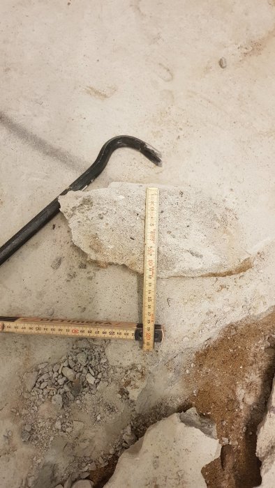 Kofot och måttstock på ett raserat betonggolv i en pågående renovering av tvättstuga.