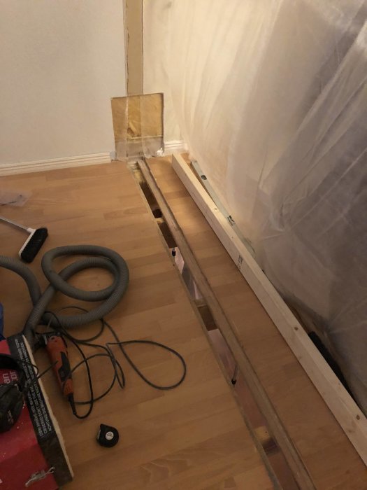 Uppskuret golvspån och exponerad balk vid vägg, med VP-rör och verktyg på golv.