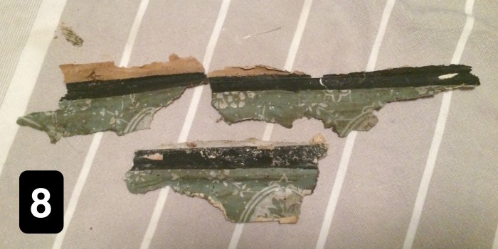 Fragment av gammal tapet med vita mönster på grön botten, numrerat 8, mot rutigt underlag.