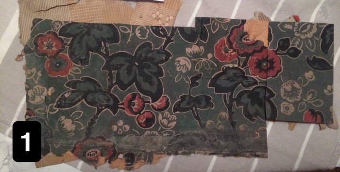 Fragmenterad historisk tapet med florala motiv i rött, grönt och beige, troligen från sent 1800-tal.