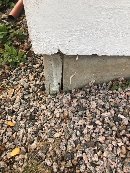 Skadat kantelement på garageplatta med synlig isolering och sprickor vid grusmark.