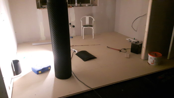Renoverat garage med nytt golv, väggisolering synlig, stol, och byggmaterial.