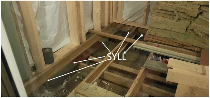 Stökig byggplats med syll på plintar och lösa lecablock under, konstruktion och byggmaterial syns.