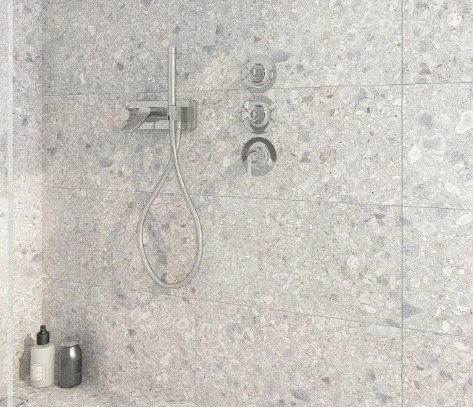 Terrazzo klinker i dusch med kromad duschstång och inbyggda kranar på väggen.