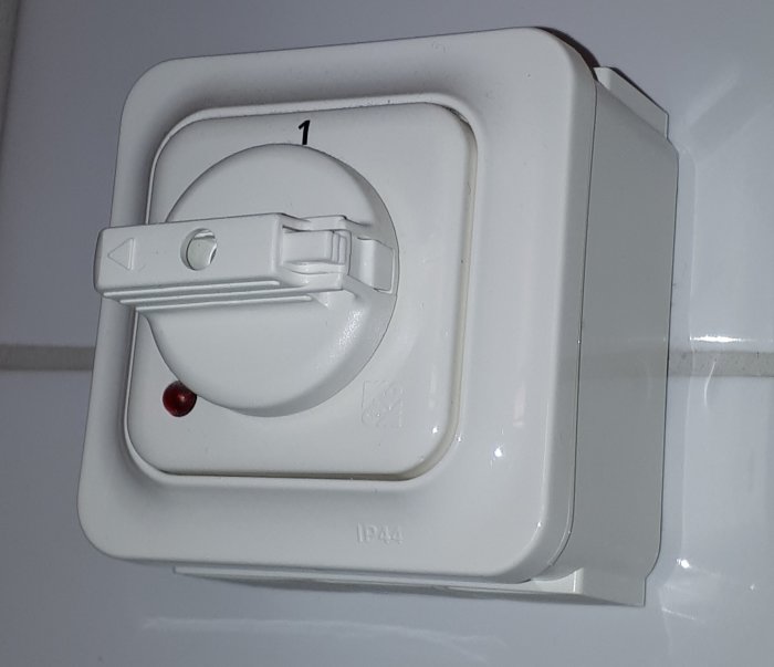 Vit kopplingsdosa för el med röd indikatorlampa på en kaklad vägg.