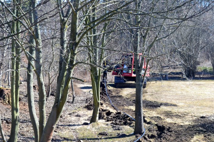 Röd kabelplog används för att gräva ner en kabel i jorden mellan träden.