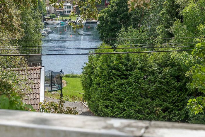 Utsikt från renoveringsprojektets hus mot en lugn vattenvy med båtbrygga och grönska.