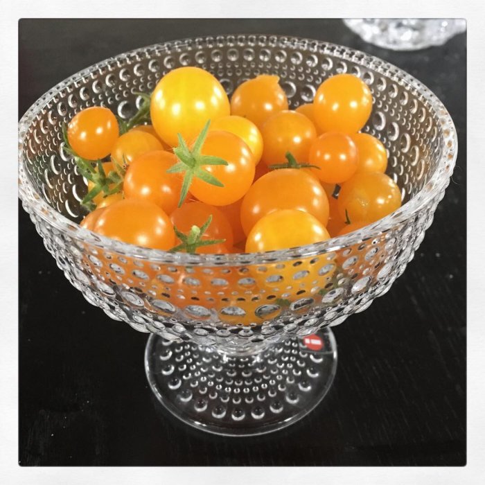 Skål med nyskördade gula och orange körsbärstomater på ett svart bord.