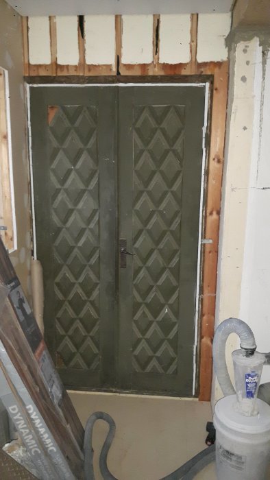 En gammal pardörr i ett renoveringsobjekt med synligt utrymme under trappan bakom.