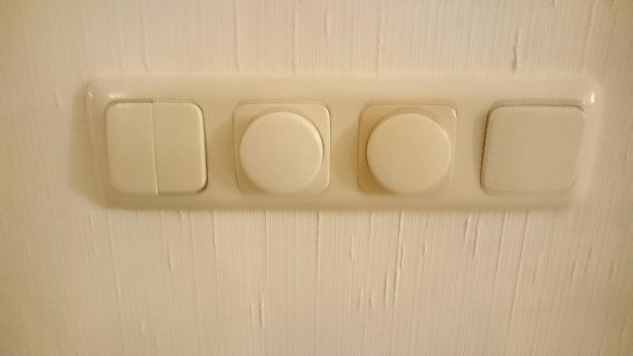 Fyra vita strömbrytare av äldre modell monterade på en vit vägg med struktur.