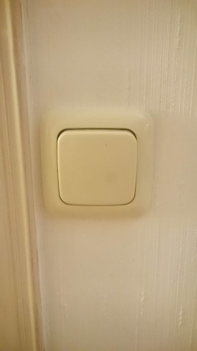 En beige väggströmbrytare från 1990-talet på en vitmålad vägg.