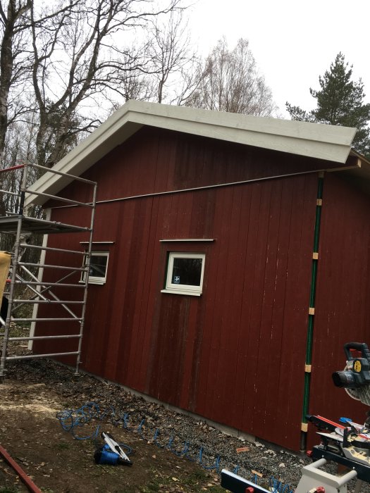 Rödmålat garage med vitt tak och byggställning, nylagt tegel på taket syns ej, byggverktyg i förgrunden.