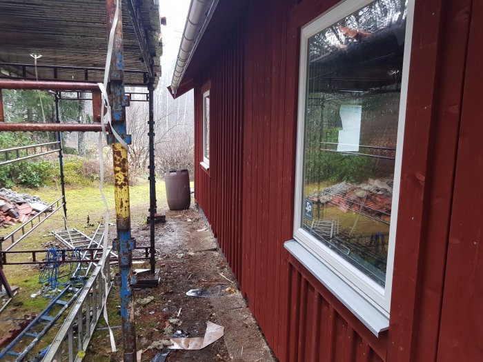 Rödfärgad husvägg med monterade, ej fastskruvade underbleck och byggnadsställning vid sidan.