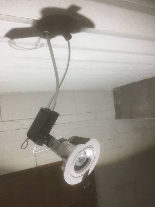 Nyinstallerad spotlights i ett takunderslag med synlig kabel och skugga på väggen.