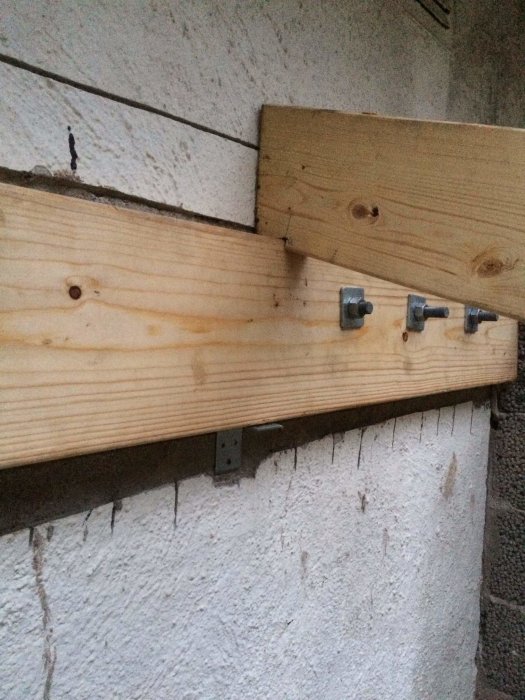 Träregel provisoriskt placerad på en vitmålad betongvägg med metallbeslag på väggen som stöd, i väntan på kapning för takkonstruktion.
