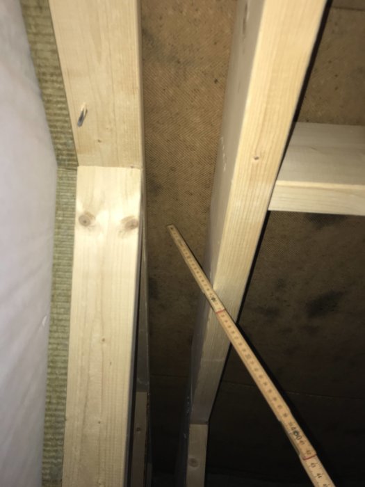 Inre takstruktur med träreglar och isolering nära en oinredd övervånings gavelvägg.