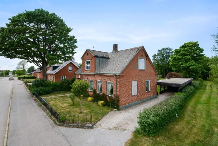 Rödtegelfasad villa med tegeltak från 70-/80-talet, carport, välbevarade trädgårdar och stort träd.